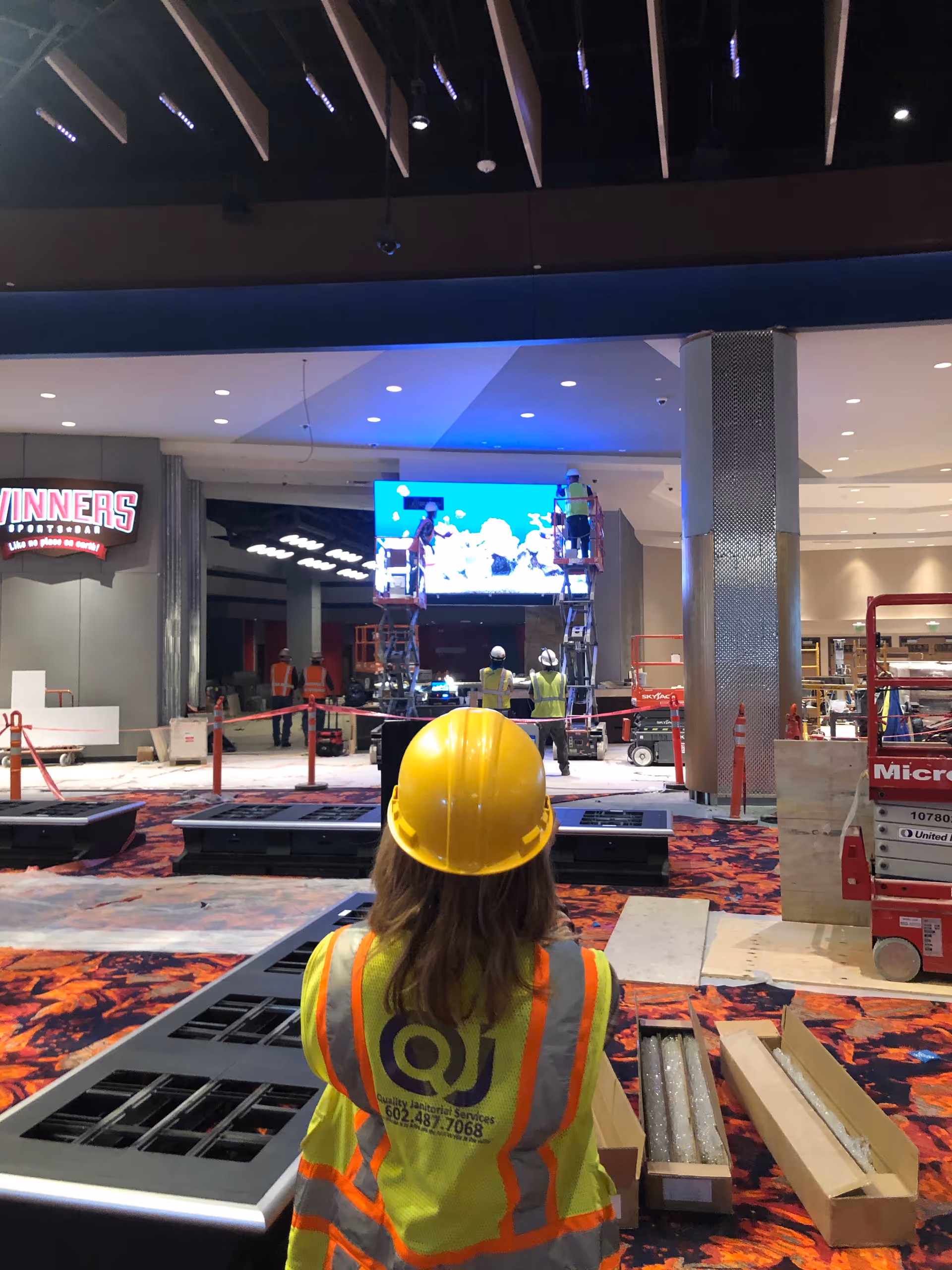 Indoor construction scene with workers in high-visibility gear and scaffolding.