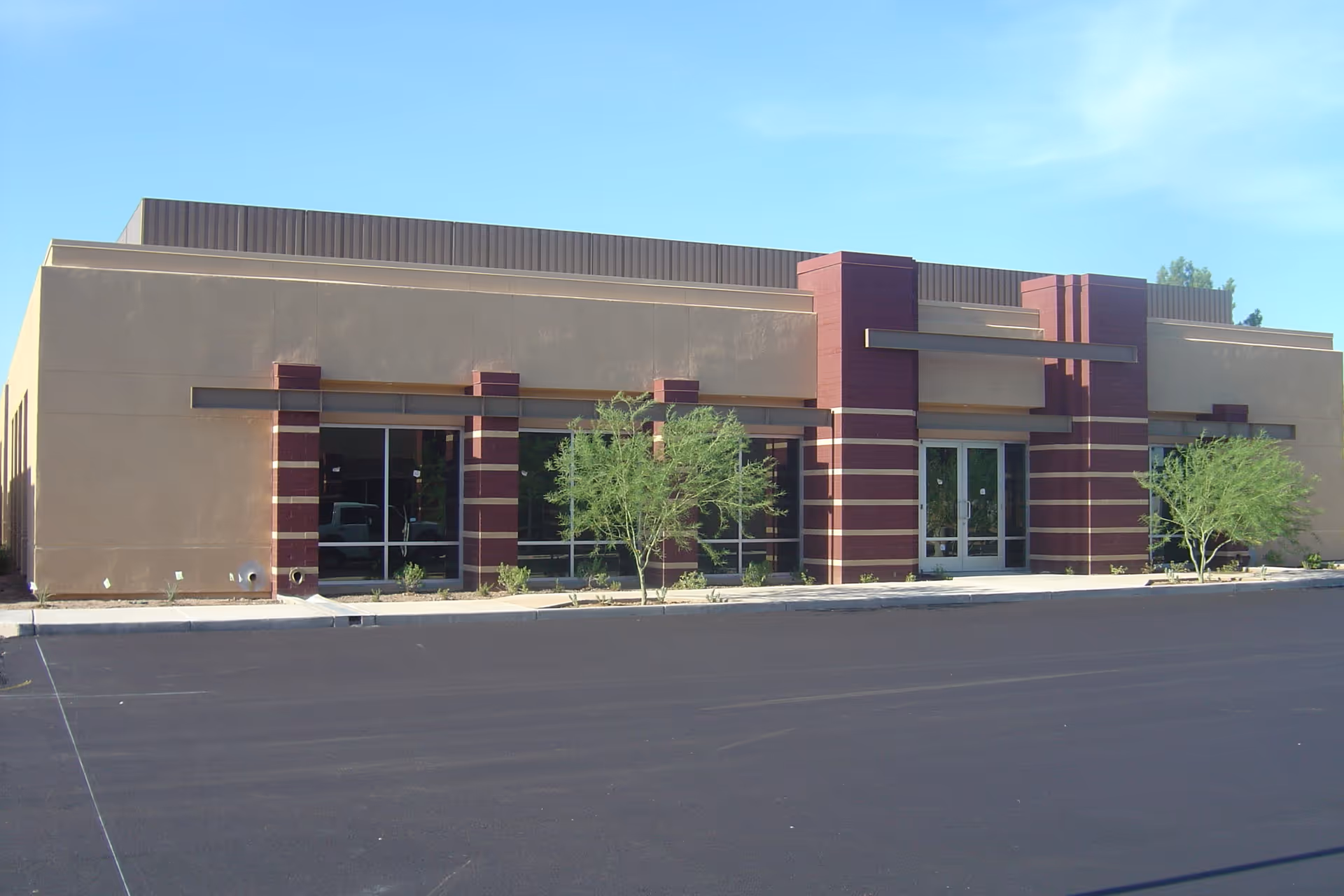 A single-story beige facility with red columns and large glass doors, empty parking lot.