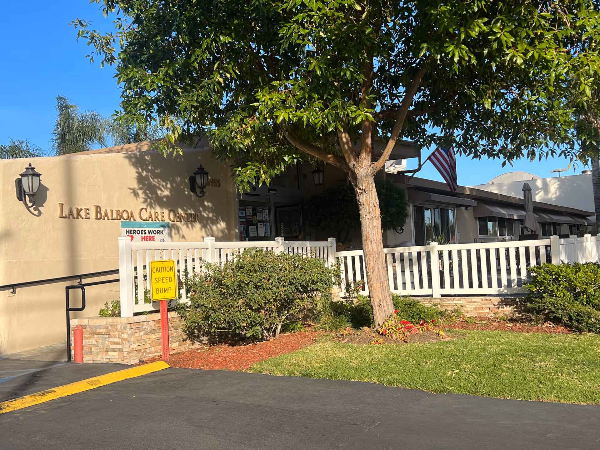 Exterior view of Lake Balboa Care Center with a white fence, trees, and entry.