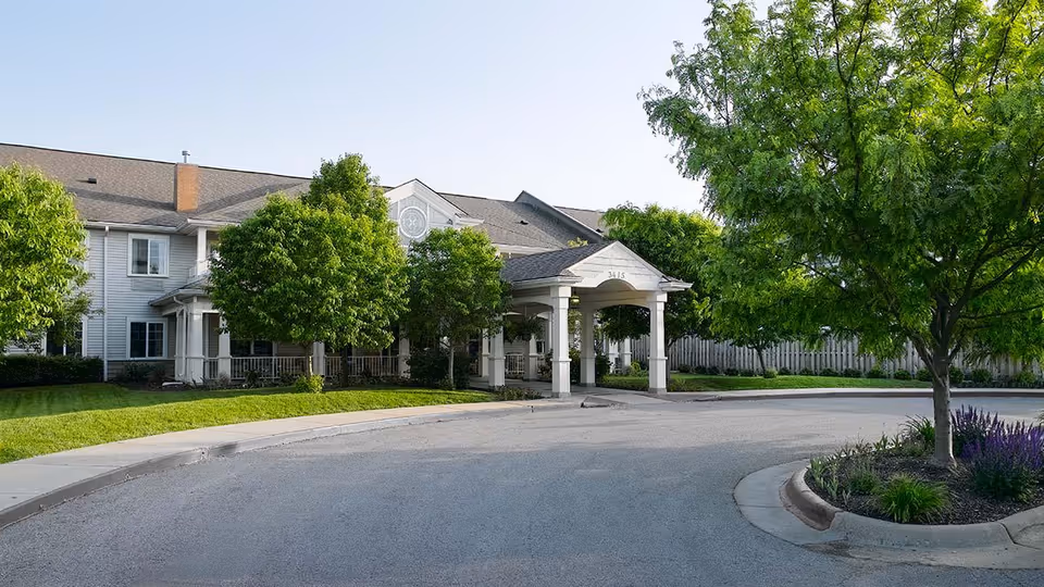 Exterior view of a senior living facility with a covered entrance and landscaped trees.