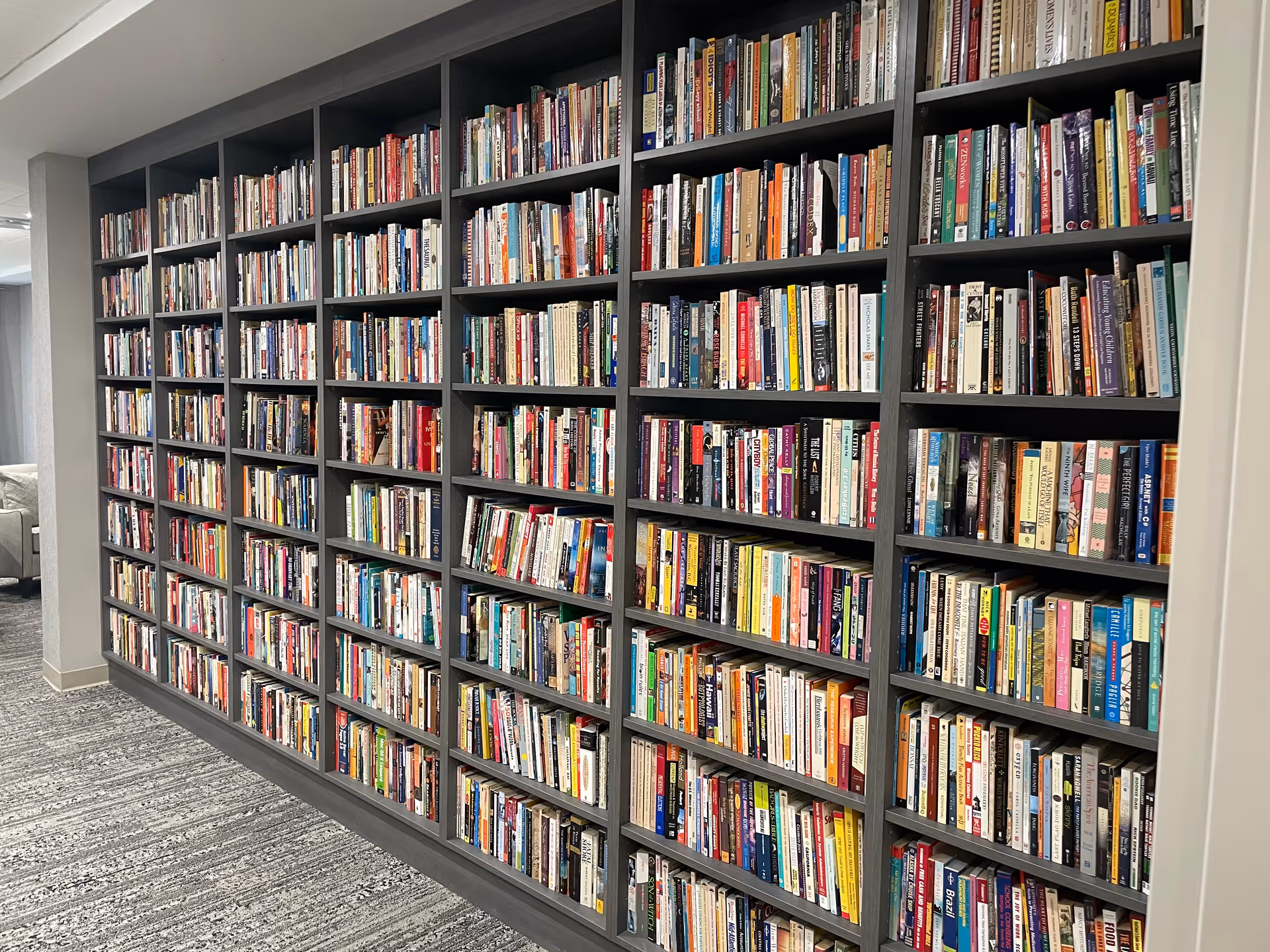 A long wall of dark bookshelves filled with colorful books in a library hall.