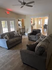 A cozy common living room with gray sofas, chairs, pillows, and open doorways