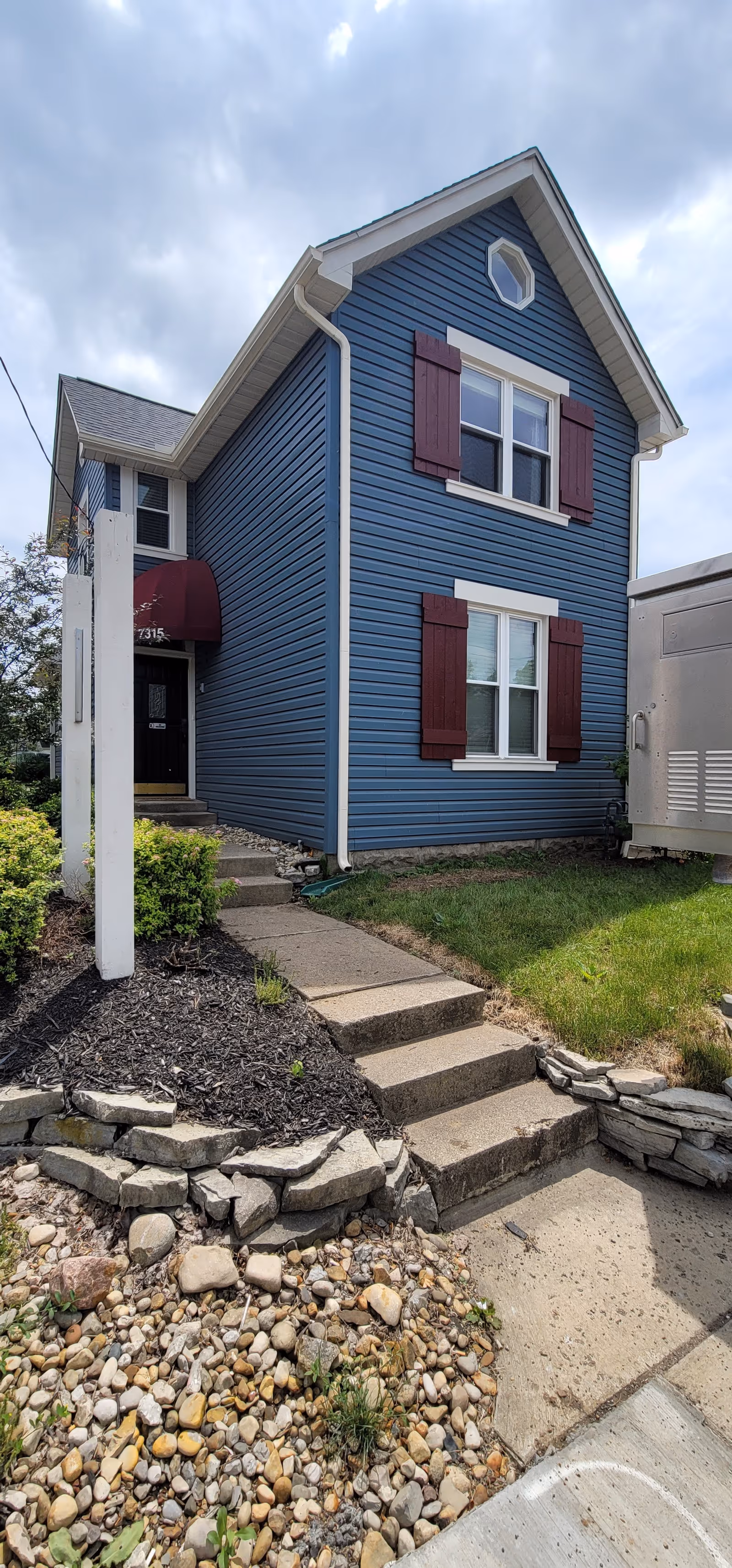 Blue two-story building with red shutters, front steps, and stone landscaping.
