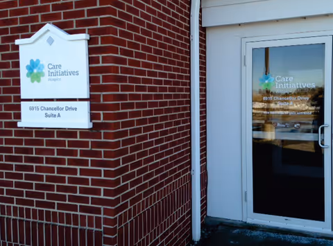 Brick exterior wall with Care Initiatives Hospice sign beside a glass entrance door.