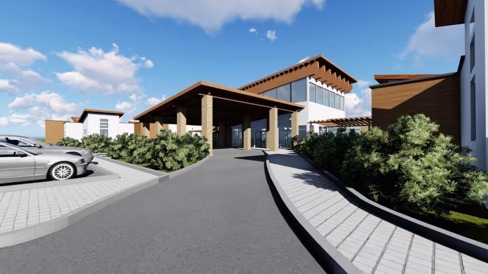 Entrance to Pointe Meadows senior living facility with driveway, greenery, and glass facade.