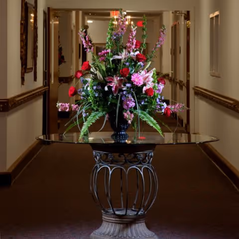 A decorative flower arrangement on a glass-topped pedestal table in a hallway.