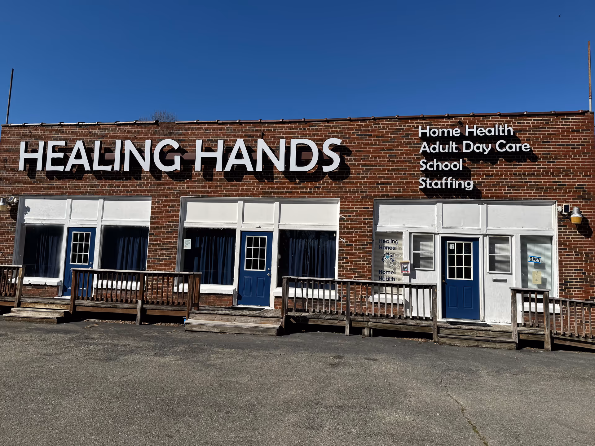Brick building with Healing Hands sign and blue doors along a wooden front ramp.
