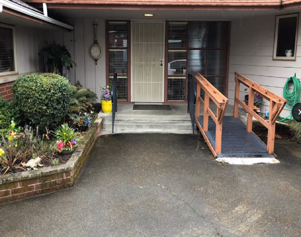 Front entrance of Bay Bridge Care Home with ramp, garden beds, and paved walkway.