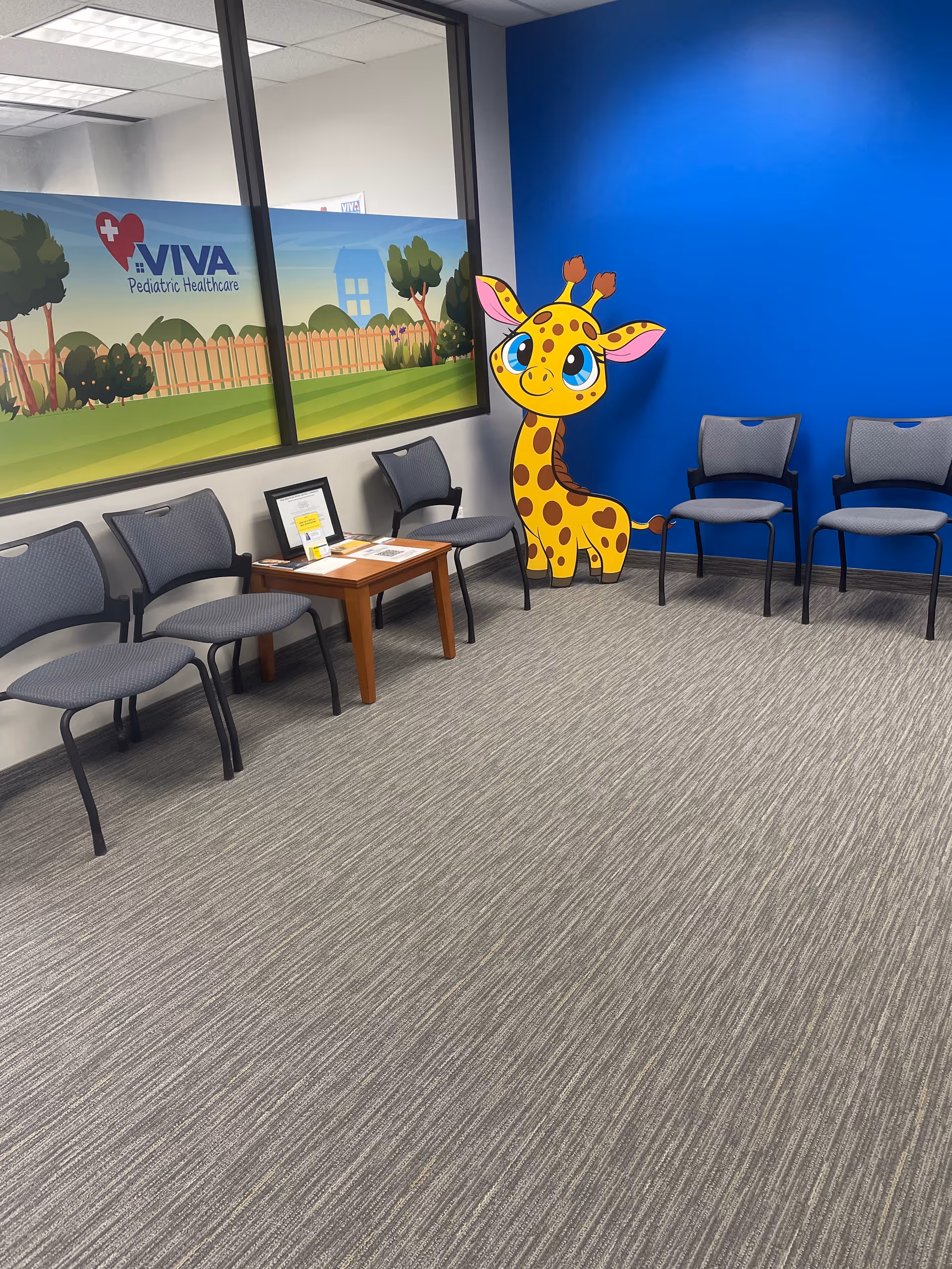 Waiting area inside Viva Pediatric Healthcare with blue wall, cartoon giraffe, and chairs.