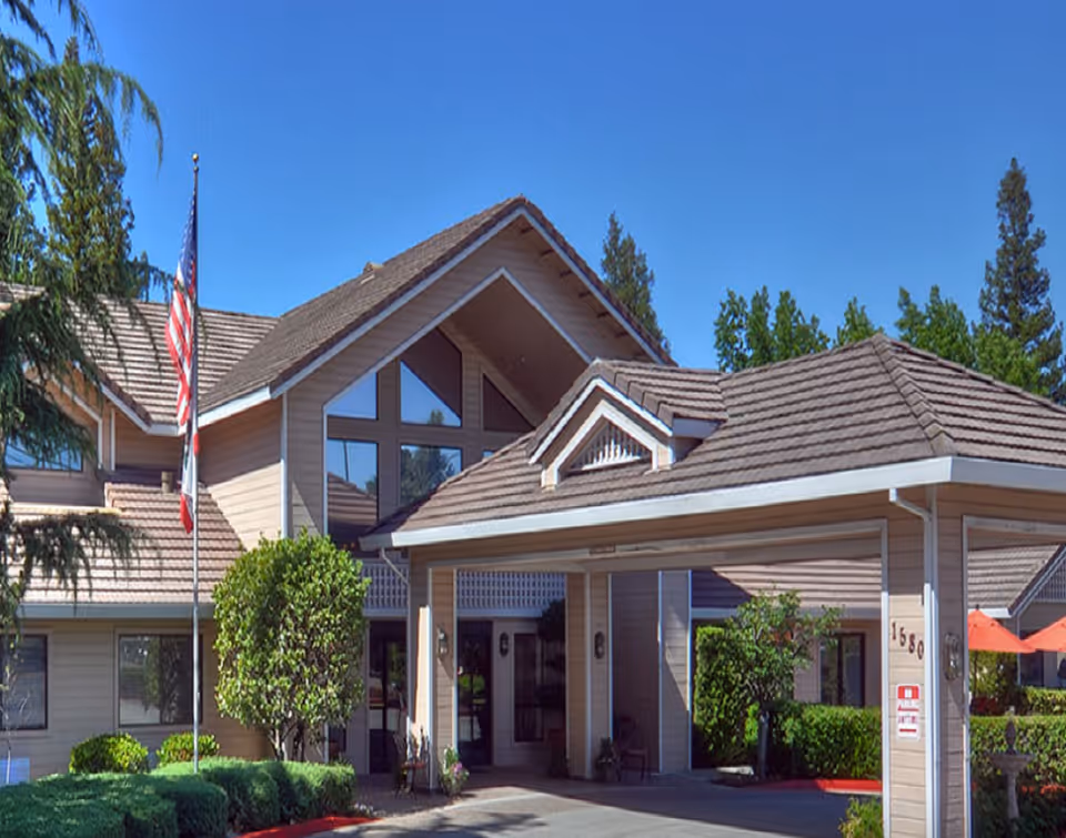 Front exterior of The Kensington at Walnut Creek, a beige senior living facility with flag.