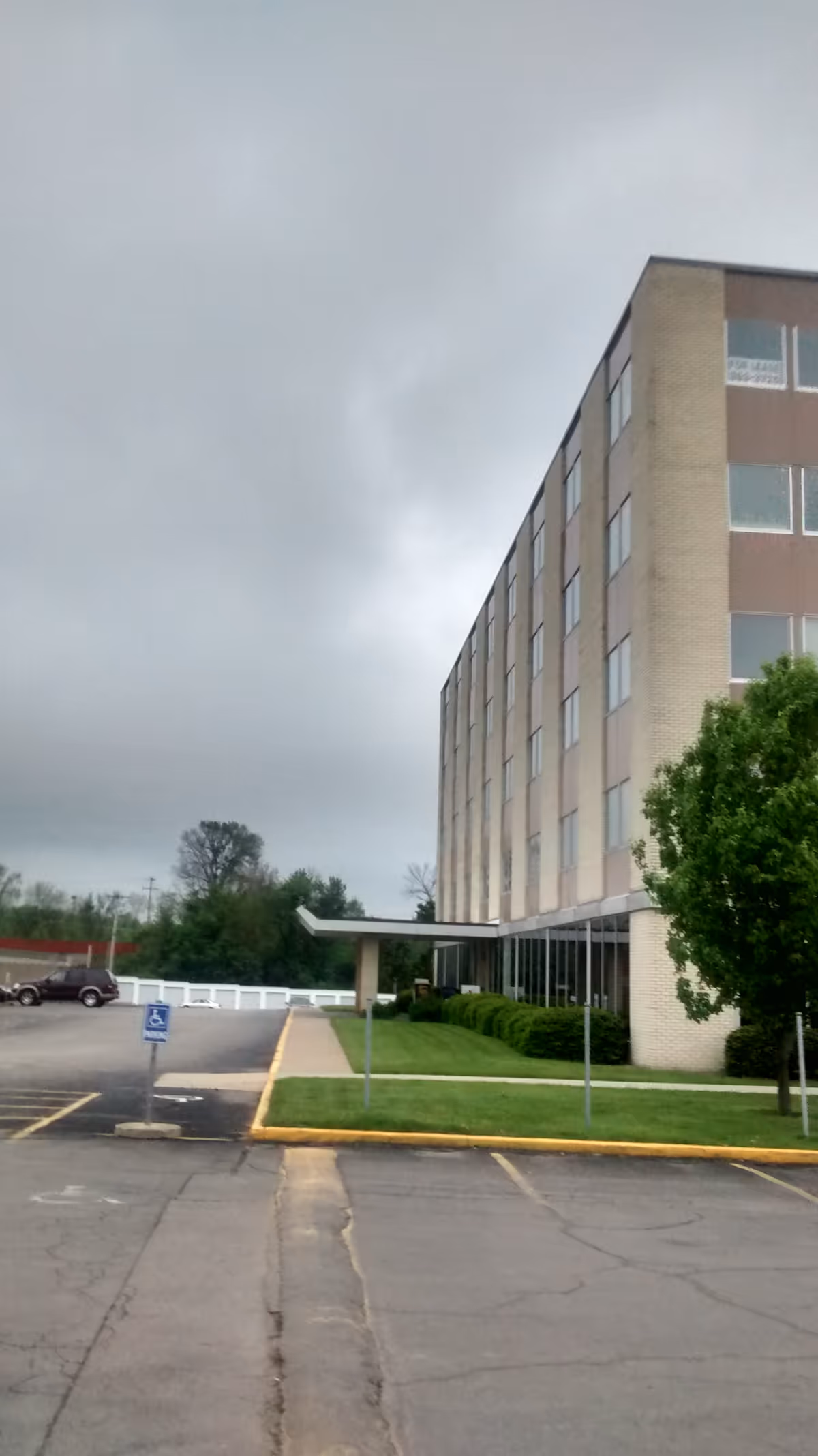 Four-story brick senior living facility exterior with entrance canopy and empty parking lot.