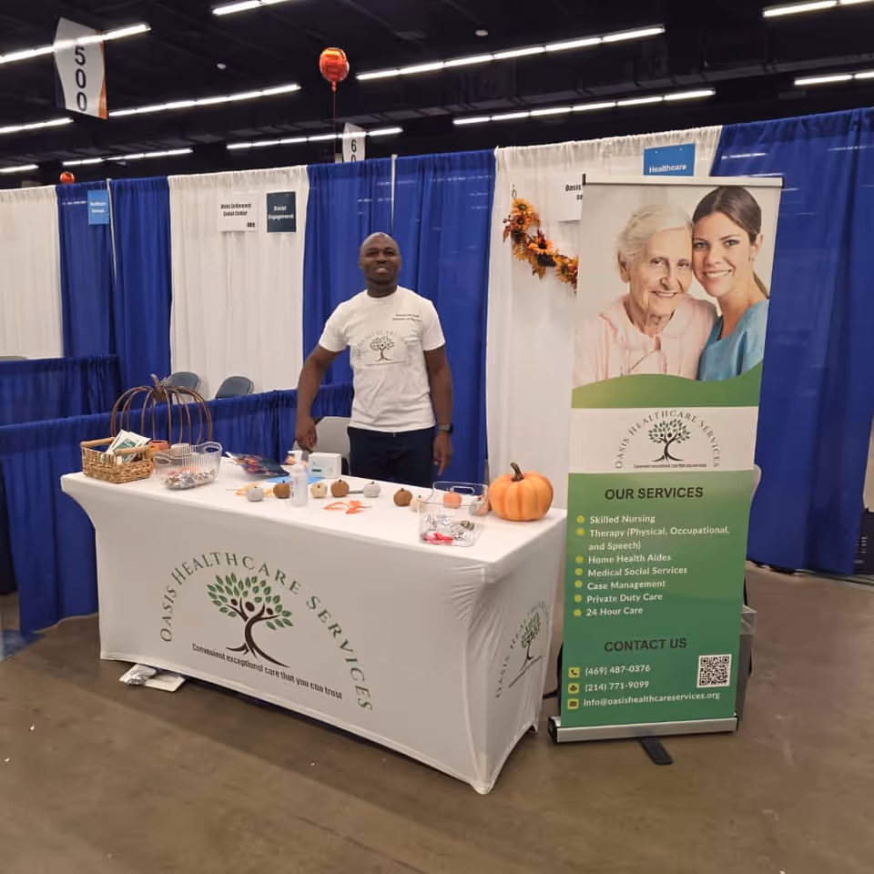 A man stands behind a table at an Oasis Healthcare Services booth in a convention hall.