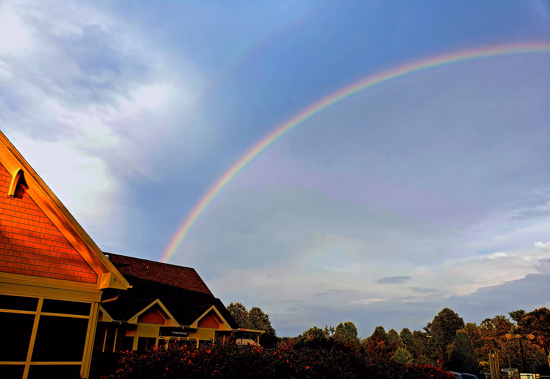 Exterior view of AMOREM building with a rainbow over the roof and trees.