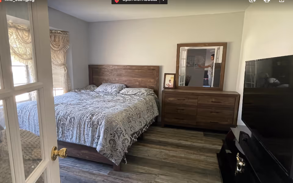 A cozy bedroom featuring a bed, dresser with mirror, and a large TV.