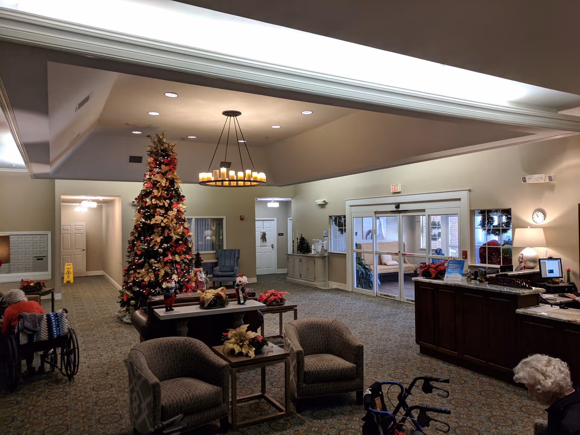 Spacious senior living lobby with a large Christmas tree, seating, residents, and a reception desk.