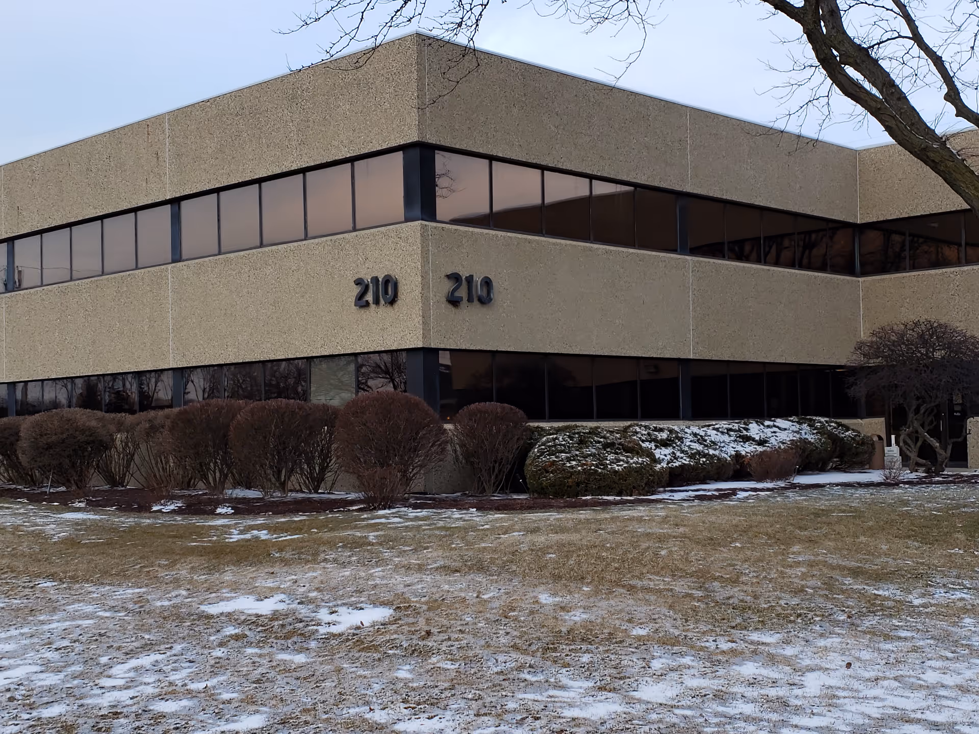 Beige building exterior with a glass window band and snow-dusted shrubs.