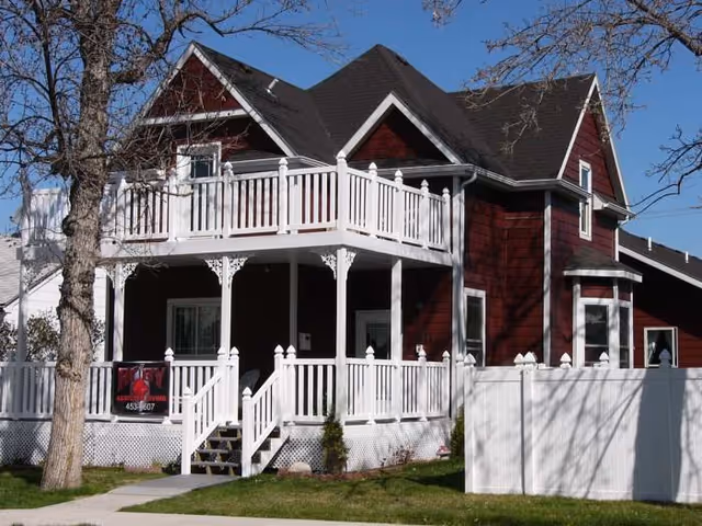 Red two-story house with white porch and railings under blue sky.
