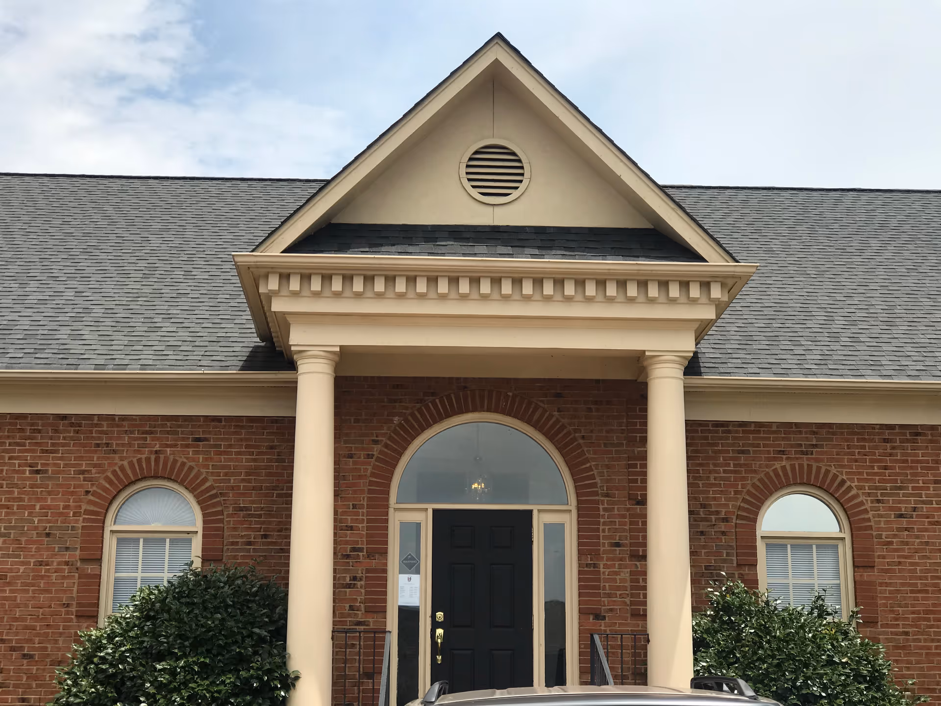 Brick building with arched windows and a covered front entrance supported by two columns.