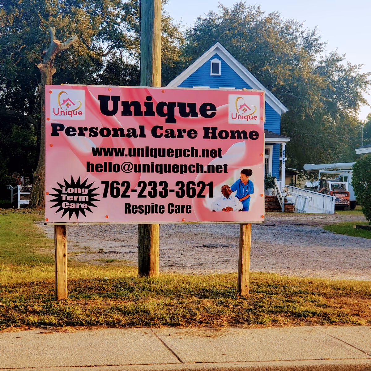 A large pink sign advertising Unique Personal Care Home sits in front of a blue house.