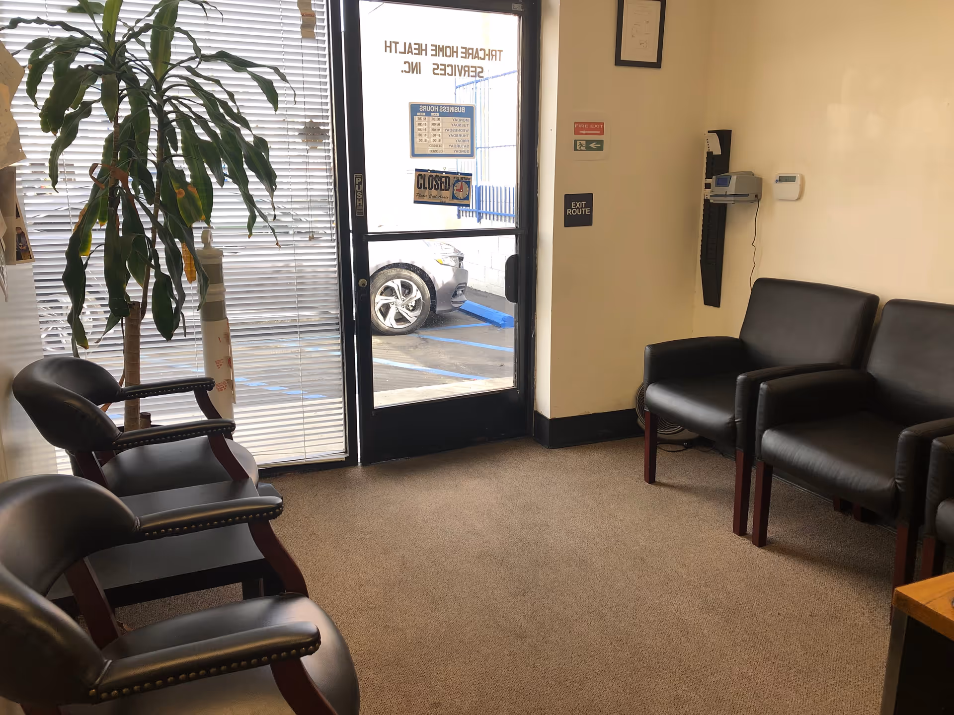 Interior waiting area with black chairs, blinds, plant, and glass entrance door.