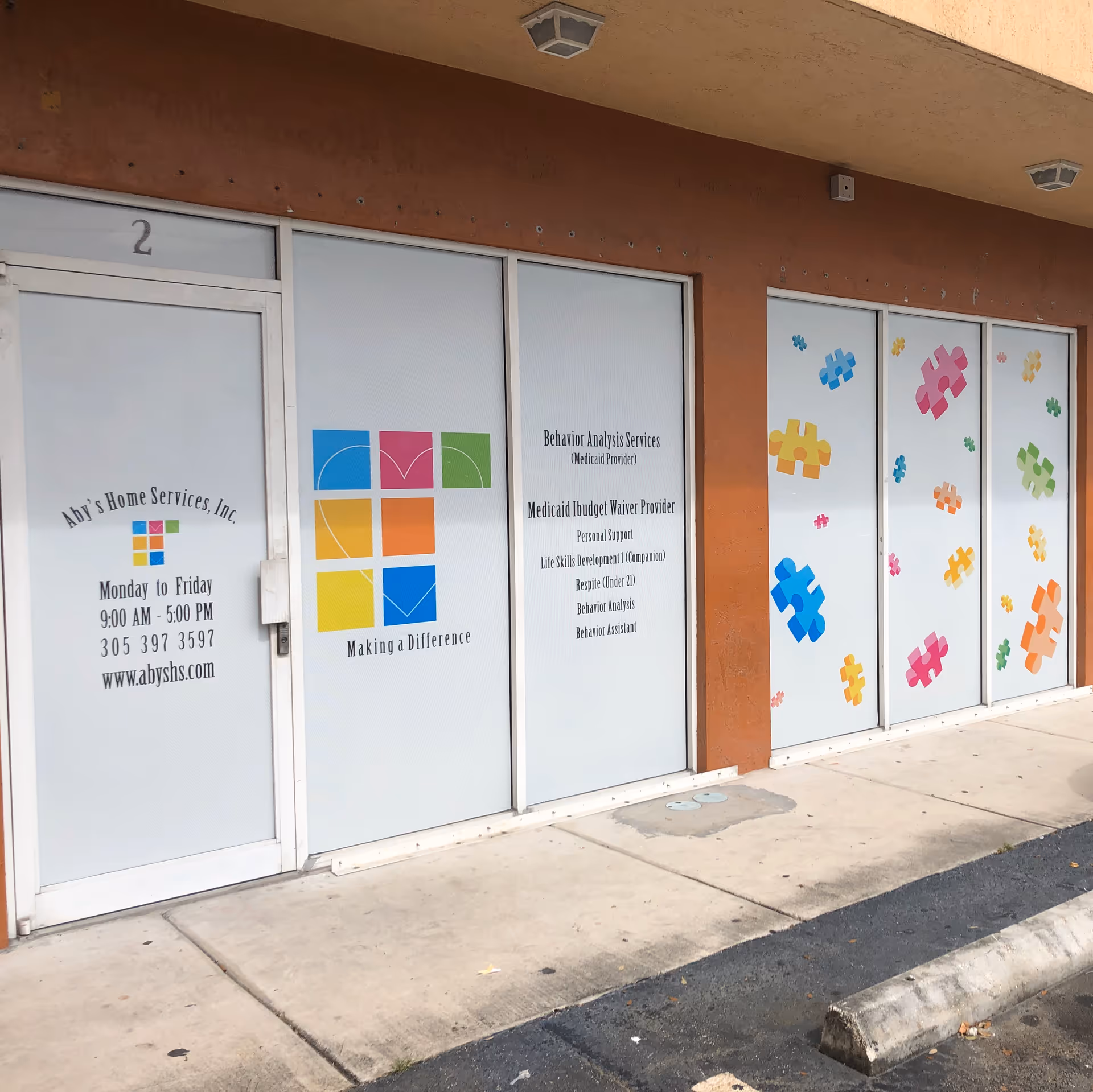 Exterior view of ABY'S Home Services storefront with colorful puzzle designs on glass doors.