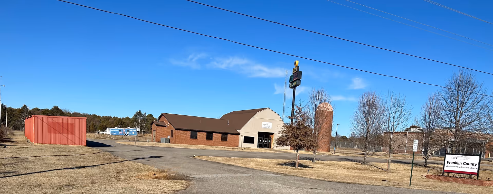 Beige single-story building with a sign, parking lot, trees, and blue sky.
