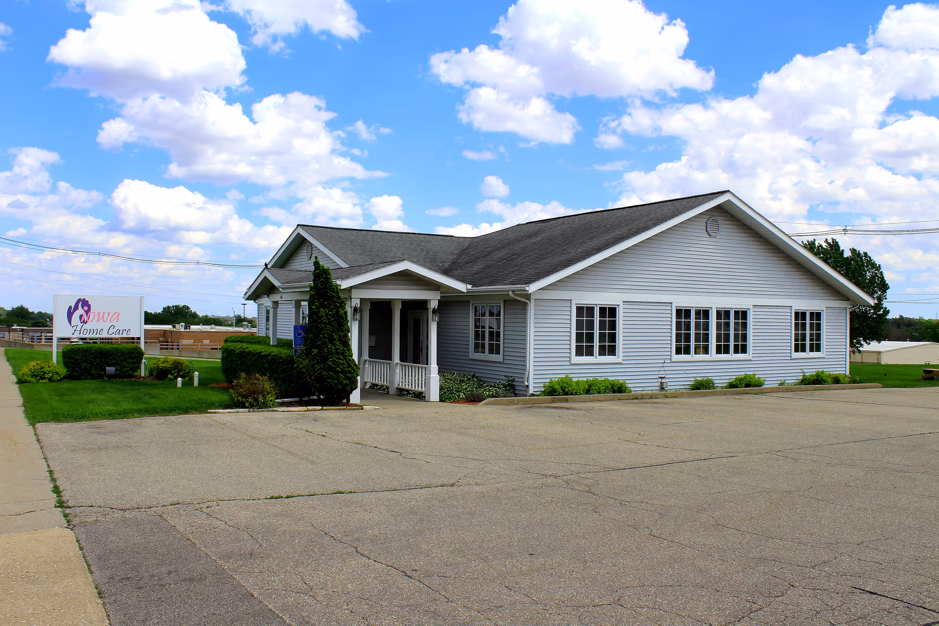 Gray single-story building with a front entrance, Iowa Home Care sign, and expansive parking lot.