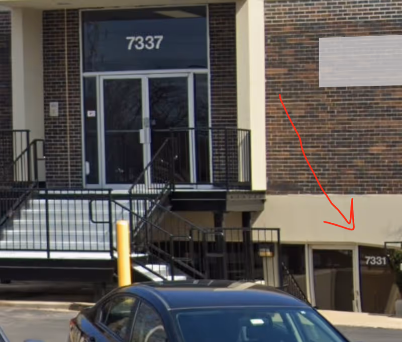 Exterior view of a brick senior living facility entrance with stairs and a car.