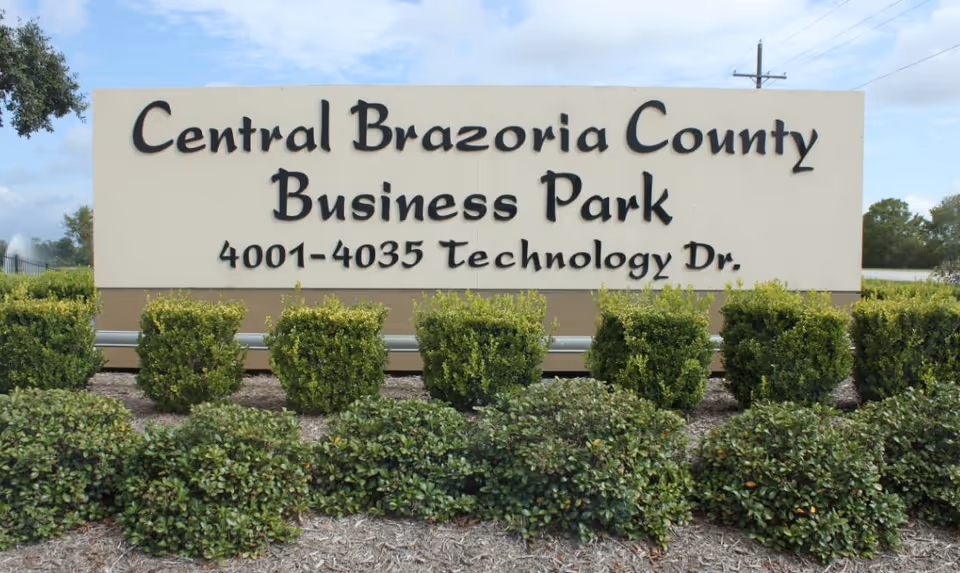 Large roadside sign reading Central Brazoria County Business Park with trimmed hedges in front