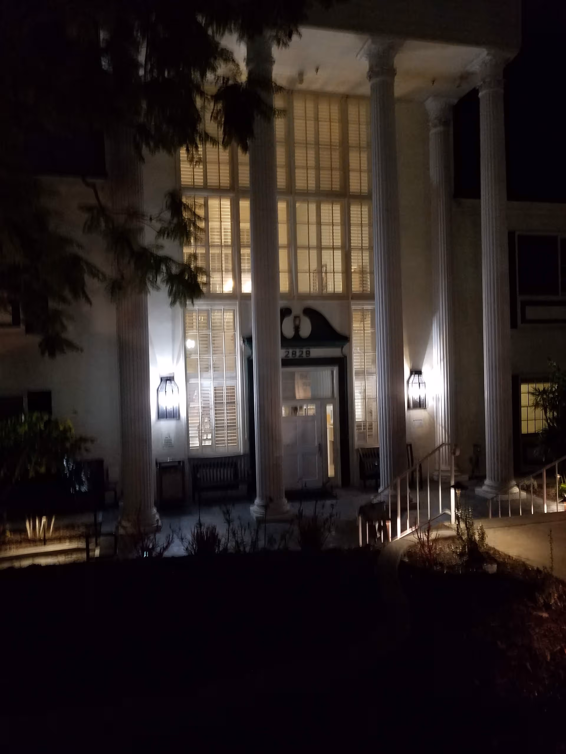 Nighttime exterior of The Shores Post-Acute entrance with tall columns and lit lanterns.