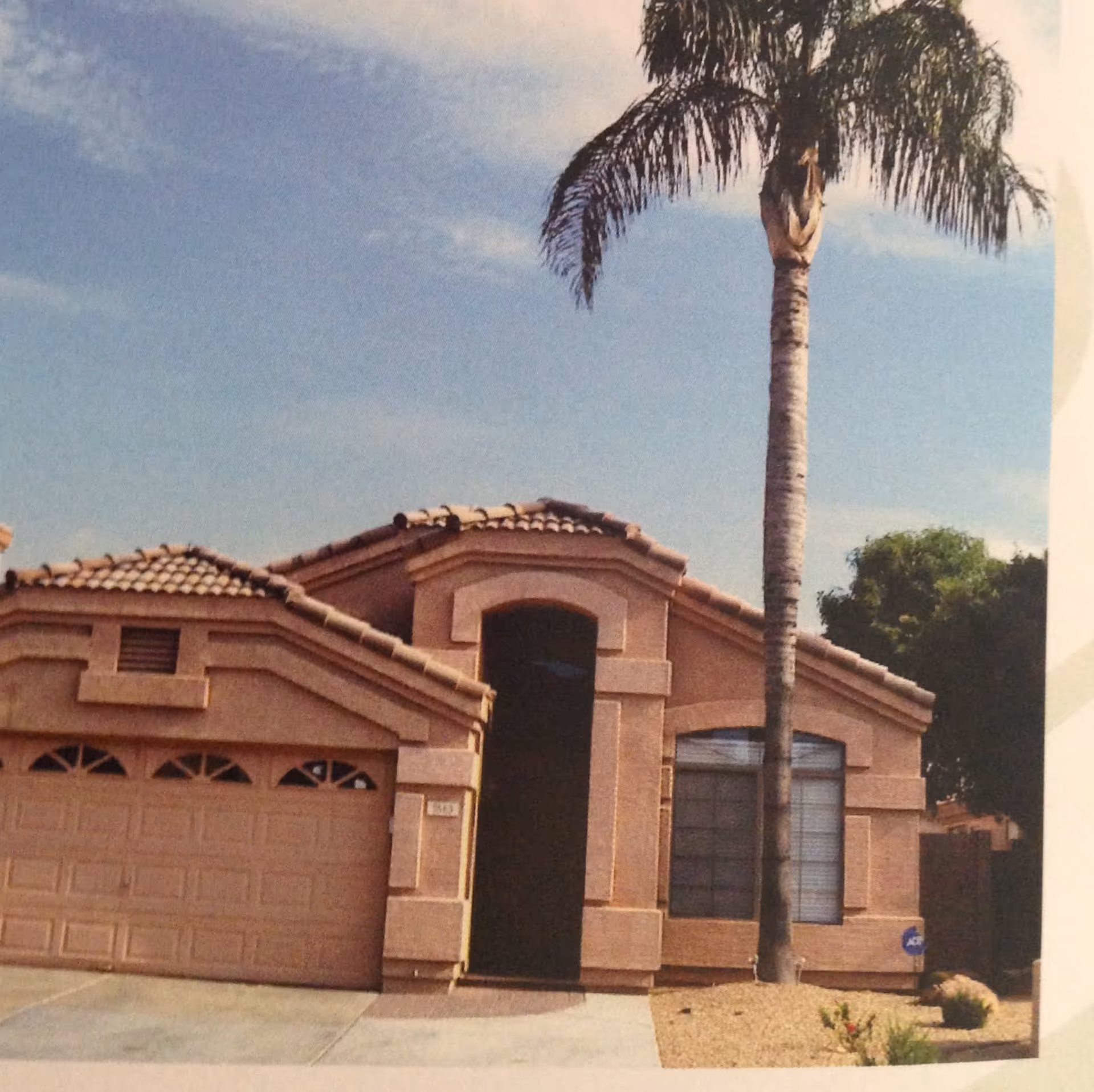Front exterior of a single-story stucco house with a tiled roof, attached garage and a tall palm tree in the driveway.