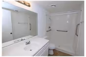 Senior living facility bathroom with sink, mirror, and accessible shower with grab bars.