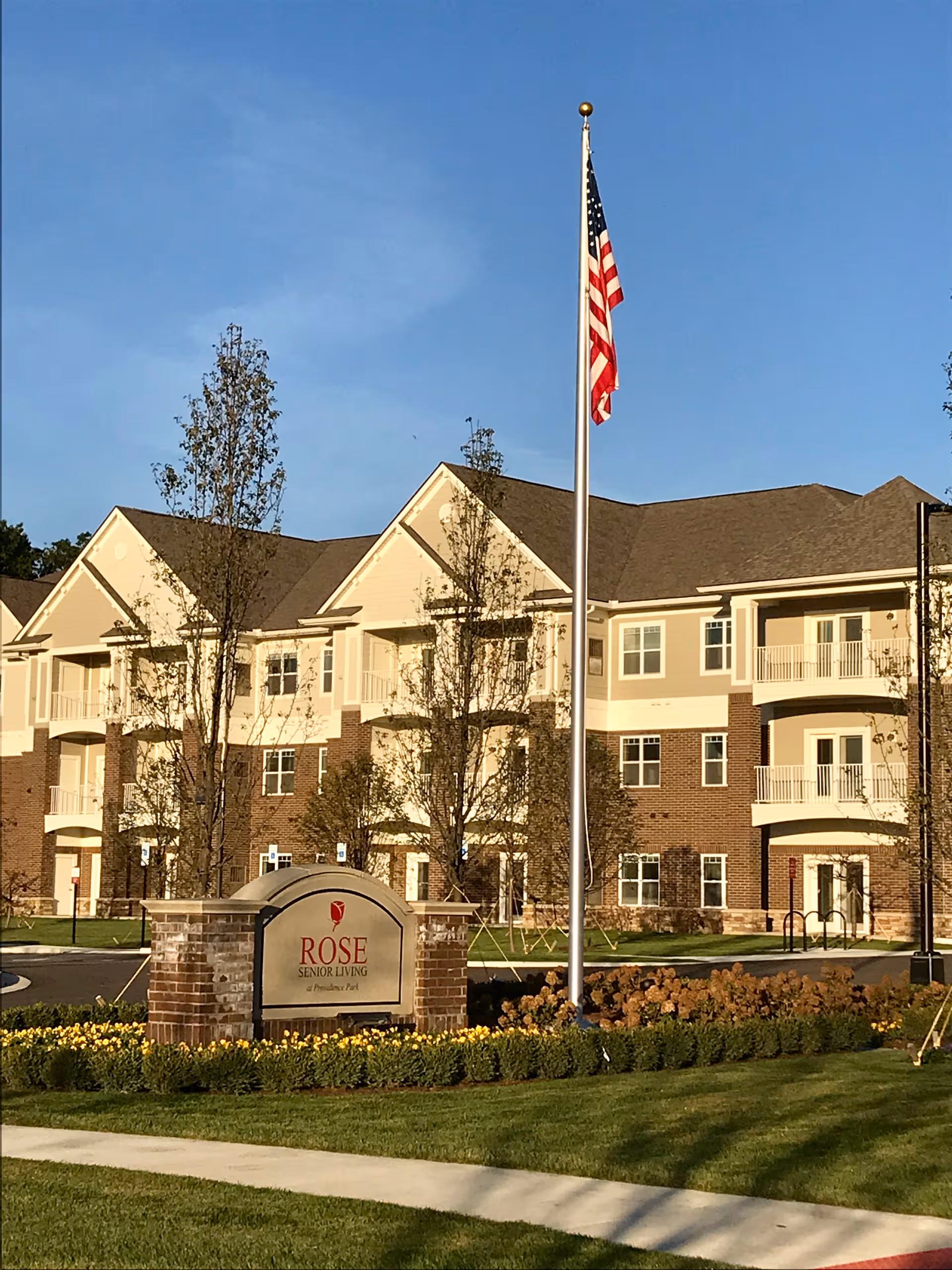 Exterior of Rose Senior Living Providence Park building with flagpole, sign, and landscaped grounds.