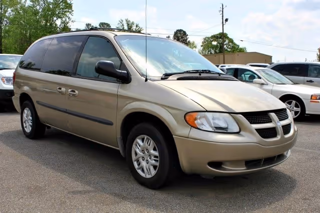 Beige minivan parked in a parking lot with other cars.