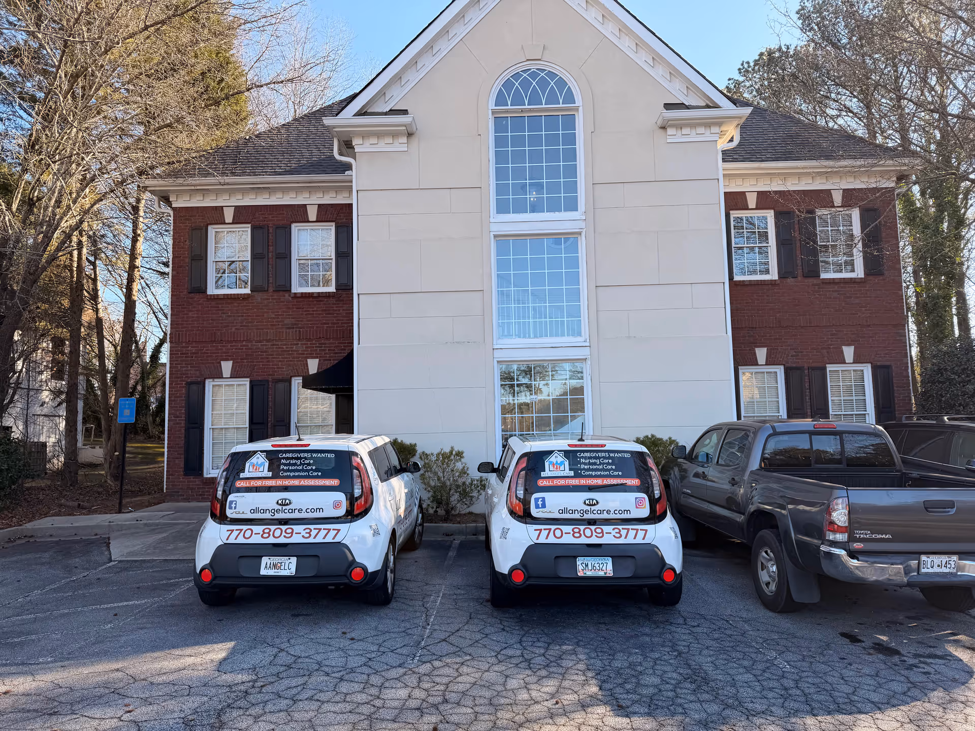 Two white vans with All Angel Care logos parked in front of a brick-and-white building.