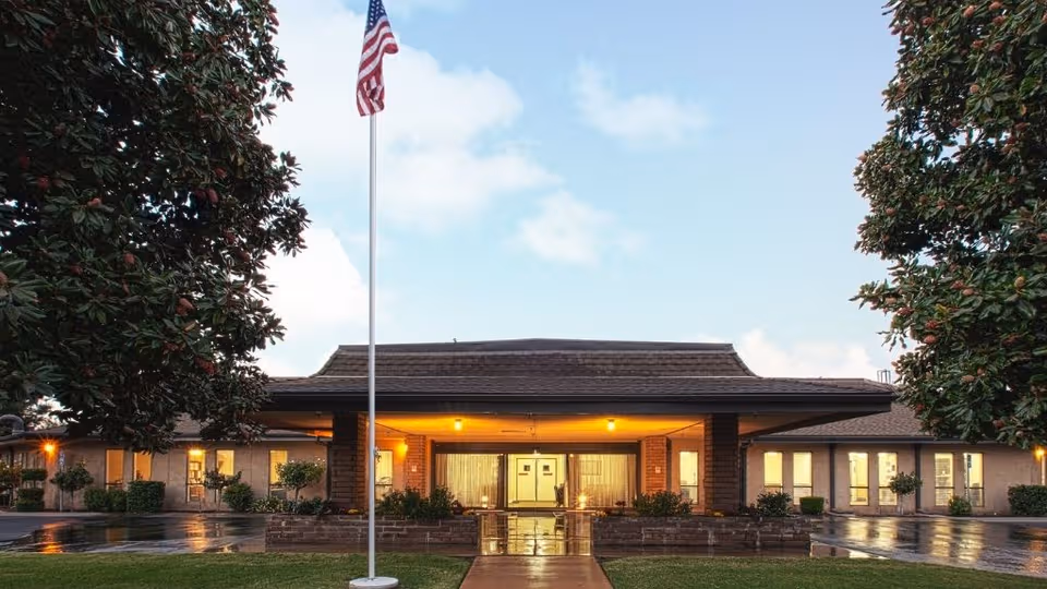 Exterior view of Linwood Meadows Care Center with lit entrance, flagpole, and landscaped grounds.