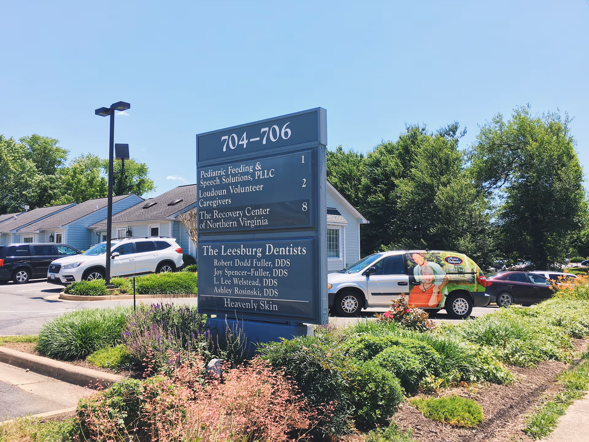 Large blue directory sign in a parking lot with a building and trees behind.
