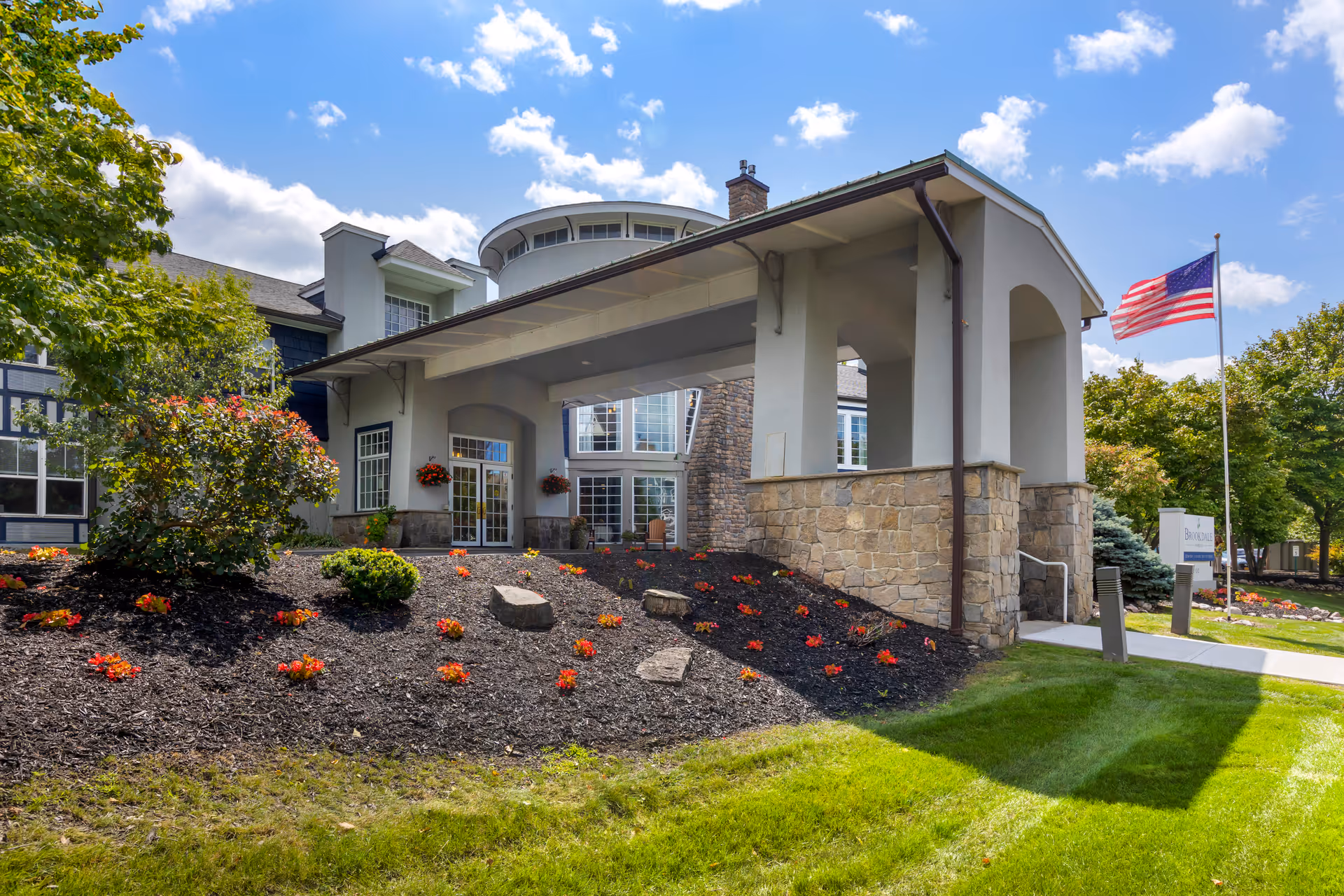 Brookdale Manlius front entrance with stone columns, covered walkway, landscaped lawn, and American flag.