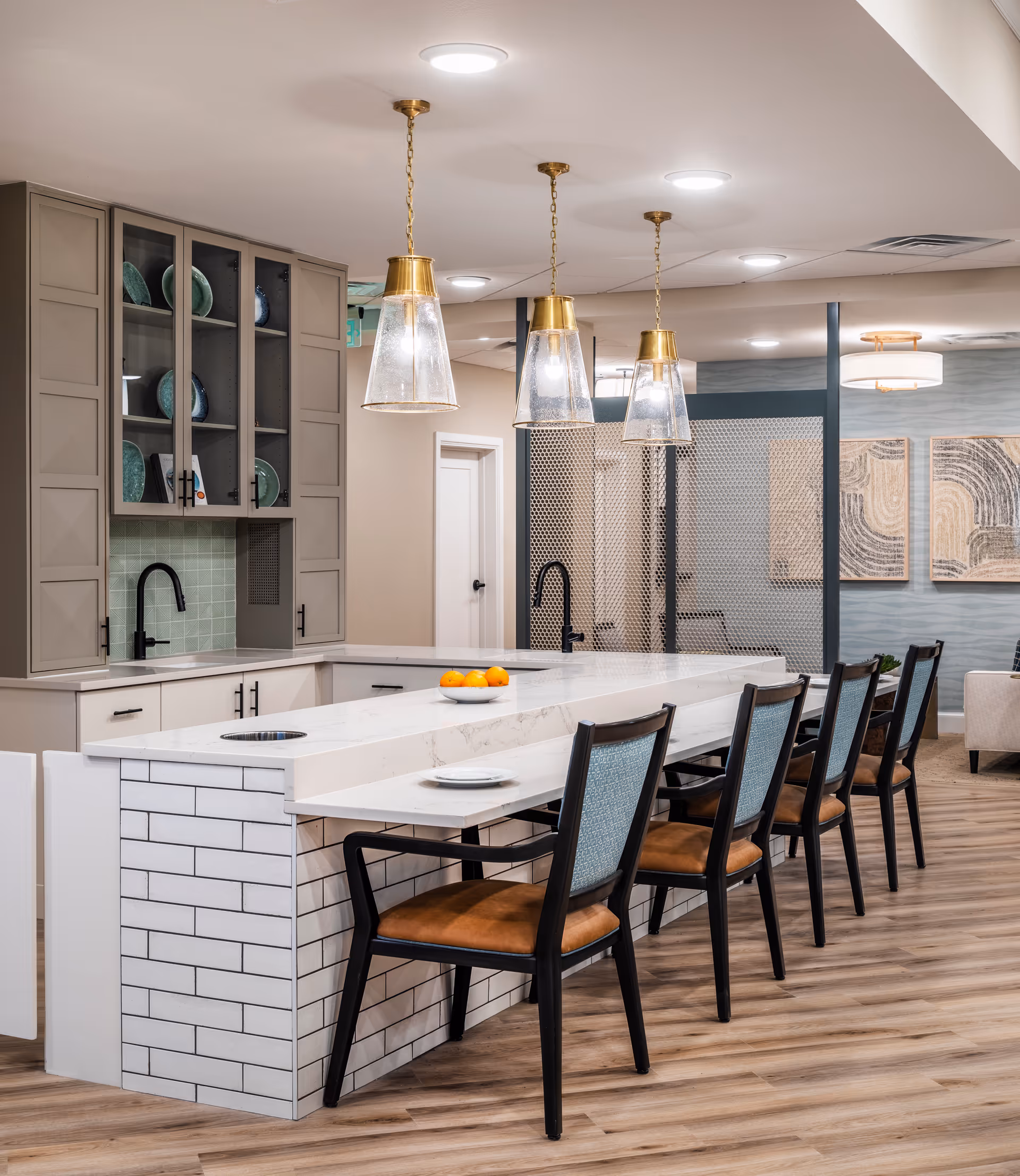 Modern kitchen island with stools and pendant lights in a senior living facility.