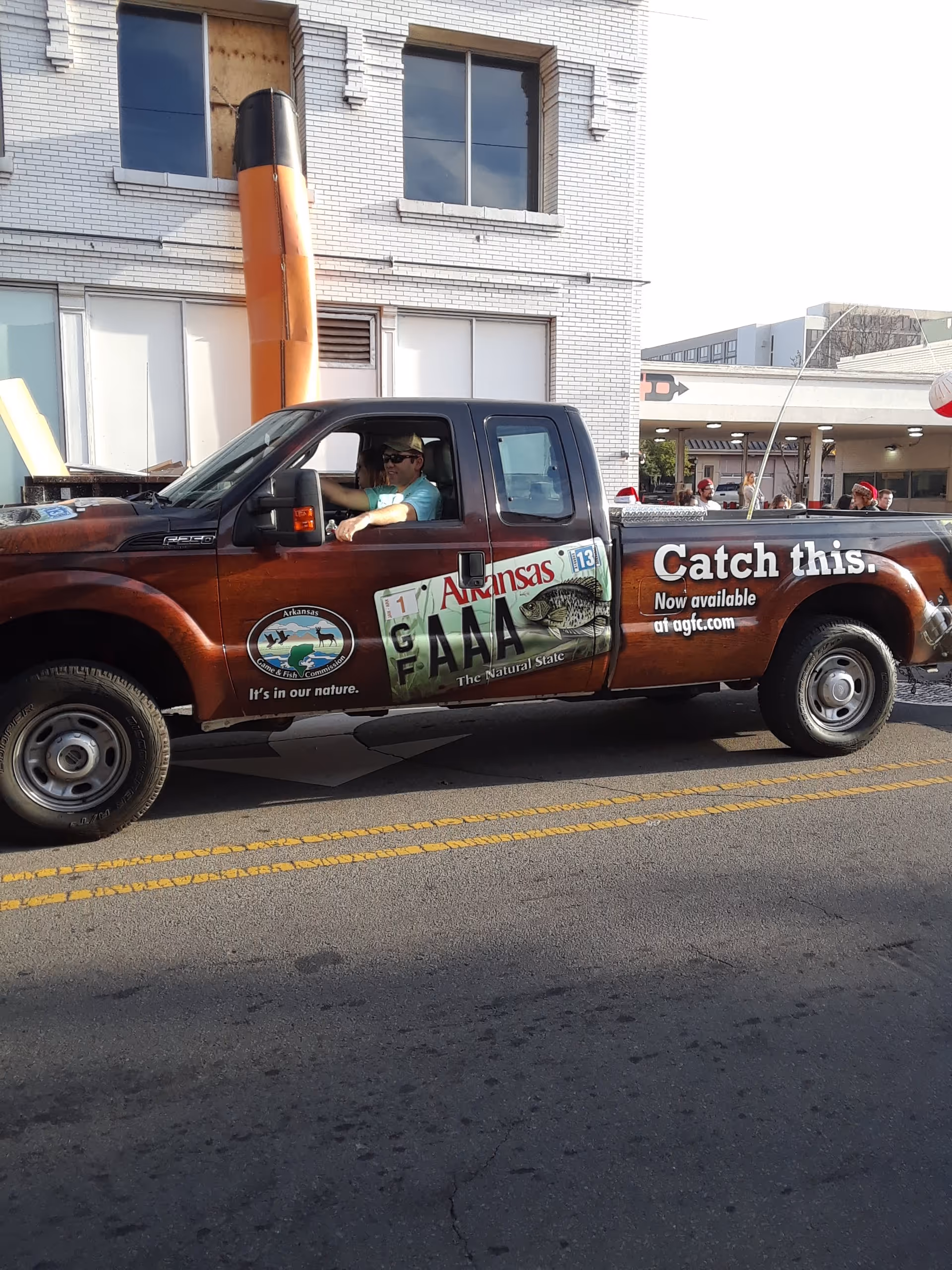 Brown pickup with promotional wrap driving past a white brick building.
