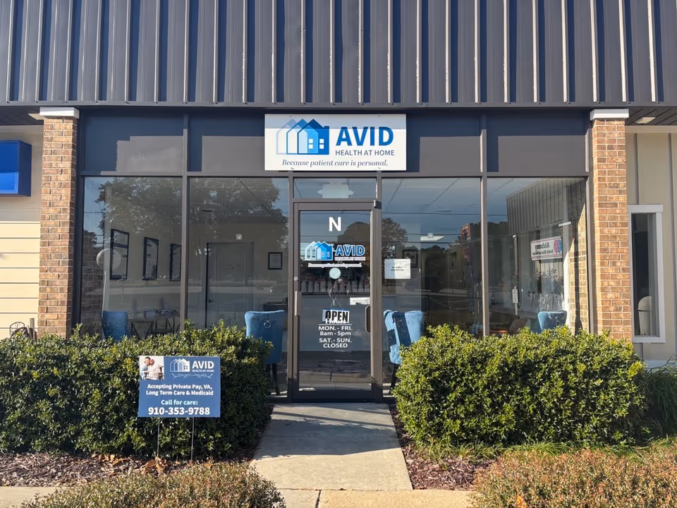 Front view of a storefront with AVID Health At Home sign, glass doors, and shrubs.