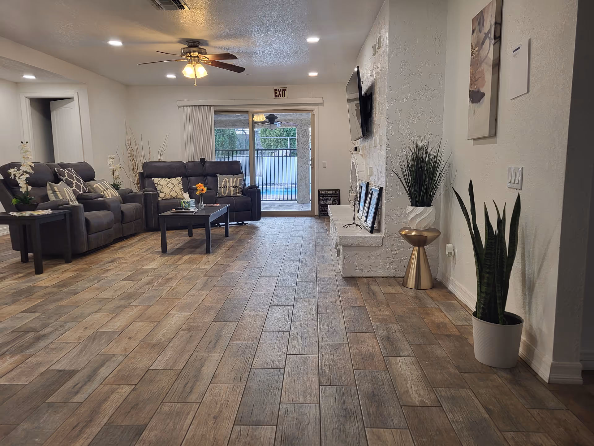 Spacious living room with gray sectional sofas, coffee tables, a wall TV, and plants.