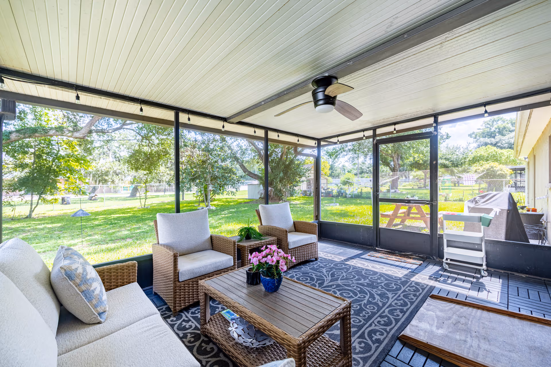 Screened outdoor patio with wicker seating, a coffee table, ceiling fan, and a green lawn beyond.
