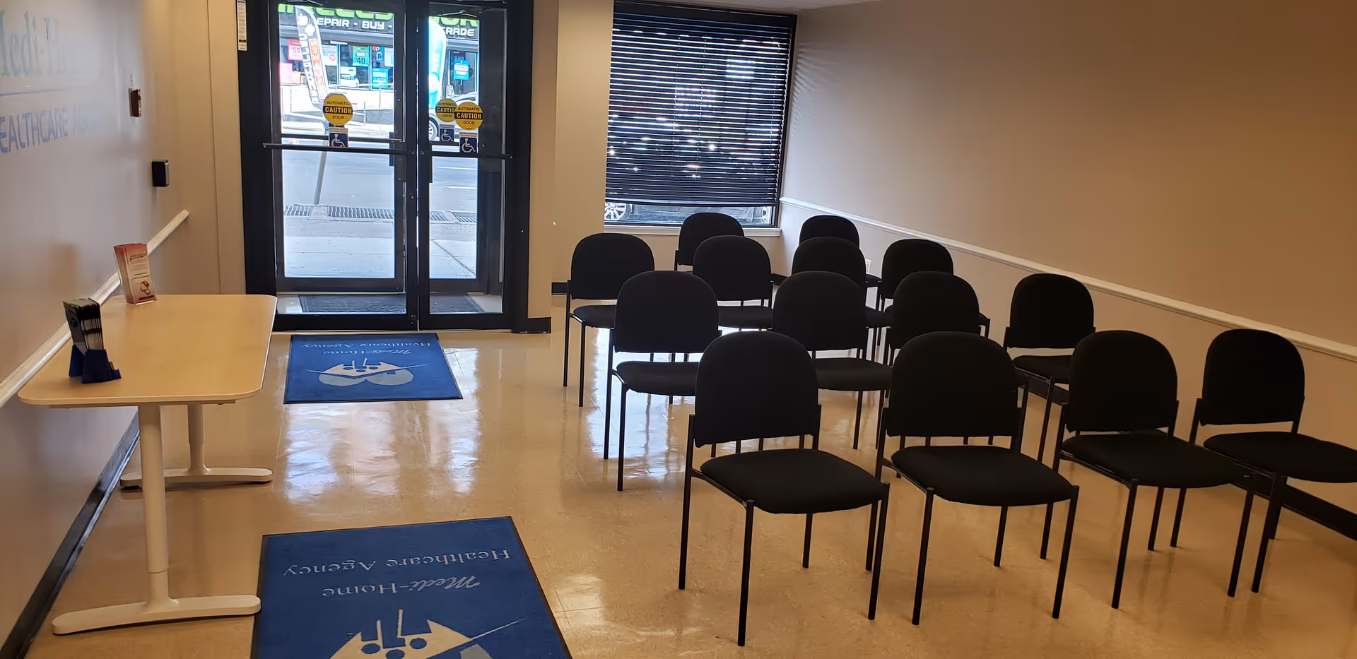 Interior senior care facility lobby with rows of black chairs and glass entrance.