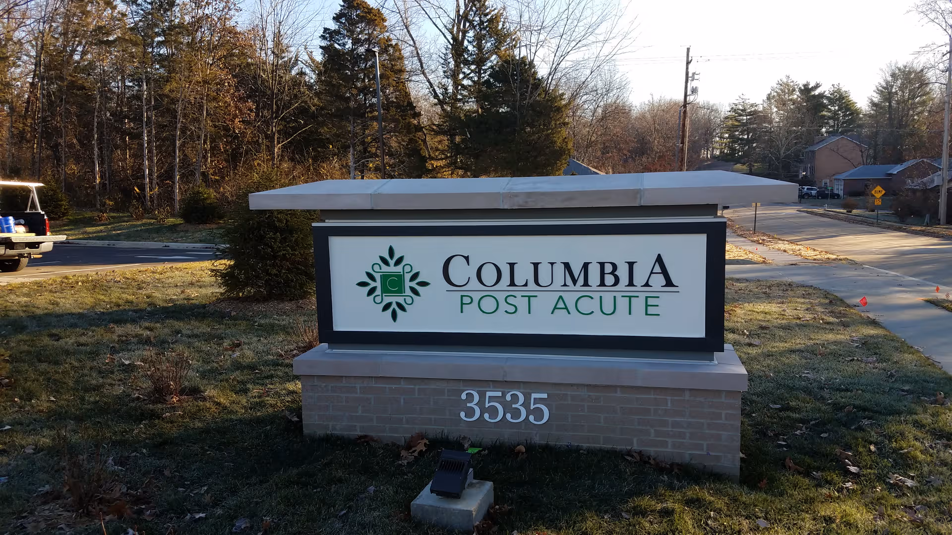 Exterior sign for Columbia Post Acute on a grassy lawn with a road and trees.