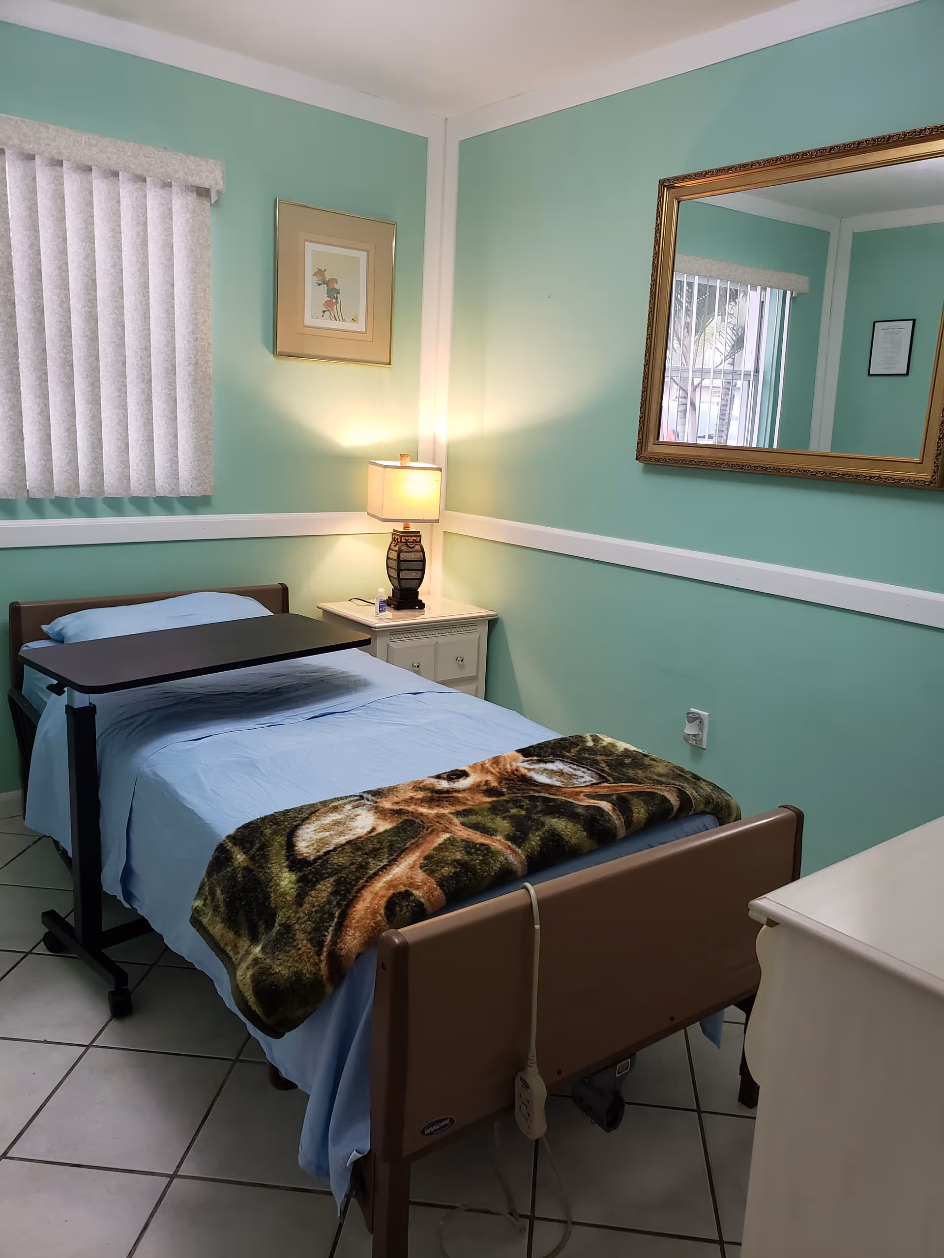 A pastel green bedroom in an assisted living facility with a bed and dresser.