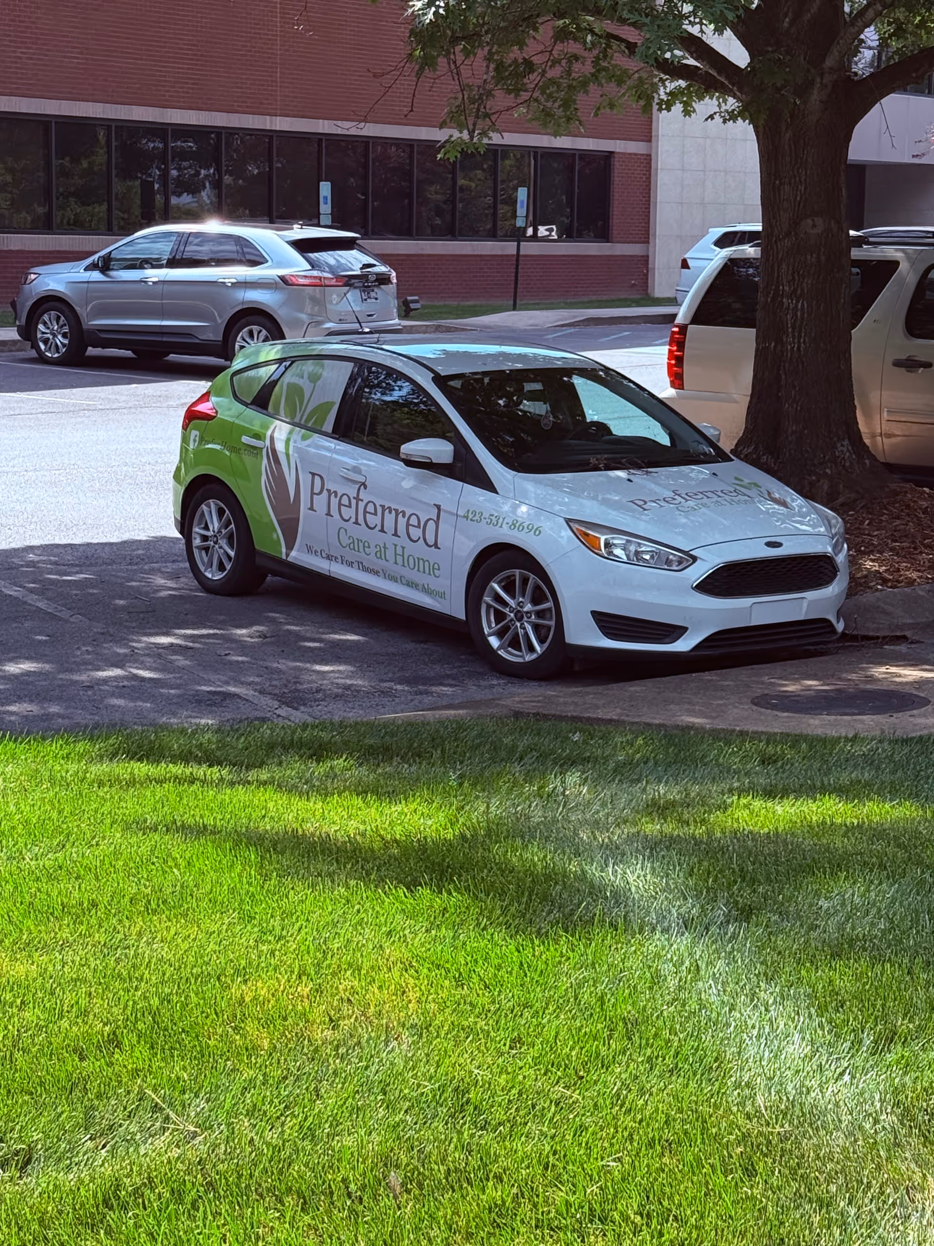 Branded white car for Preferred Care at Home parked in a lot near a brick building.