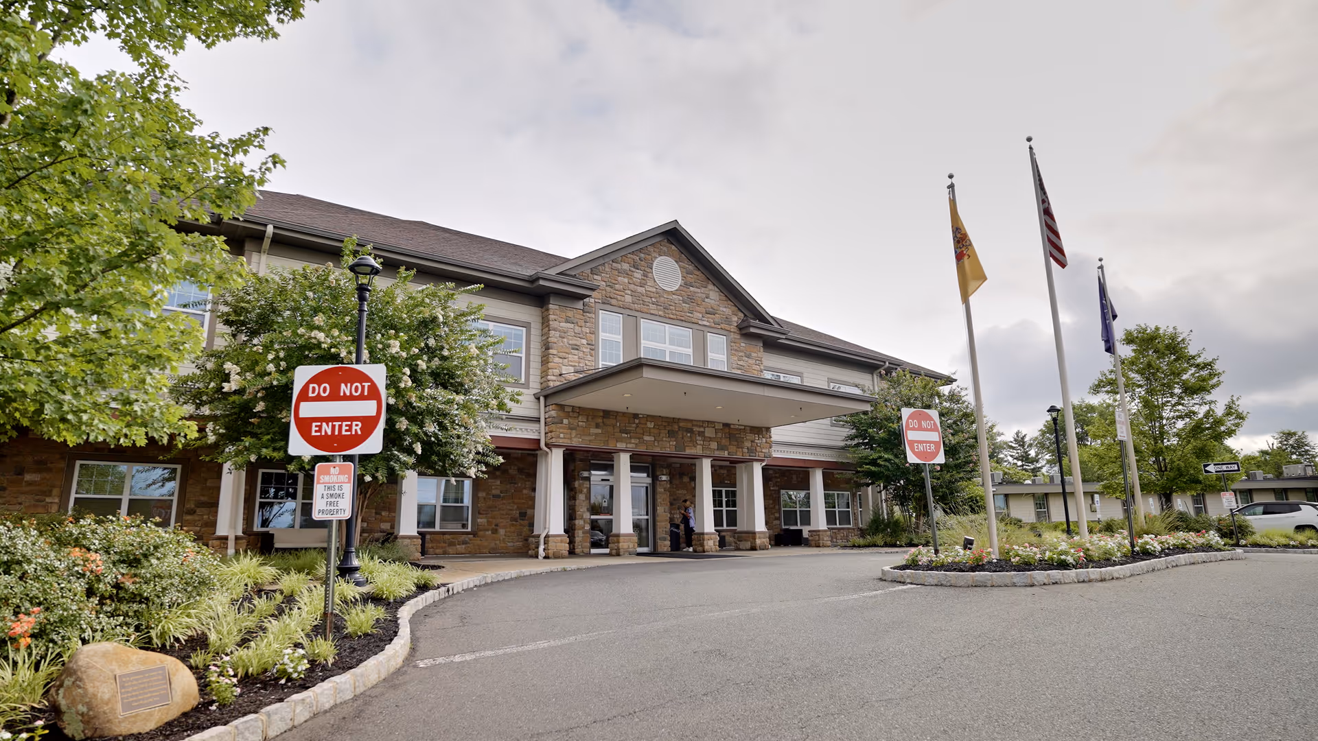 Assisted living facility exterior with stone facade, entrance canopy, and flagpoles.