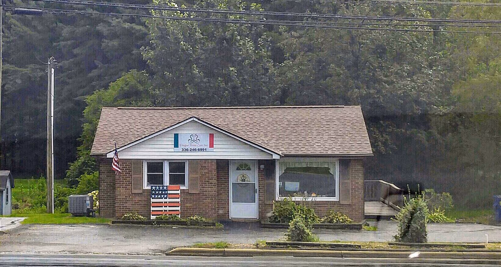 Single-story brick building labeled Unique Care Inc with flag and window display