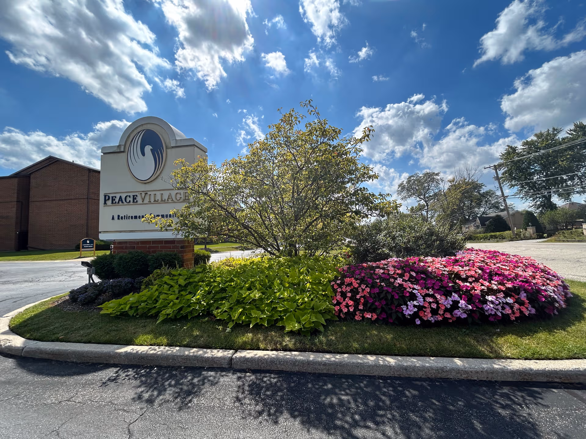 Front exterior of Peace Village with landscaped flower beds and a large sign.